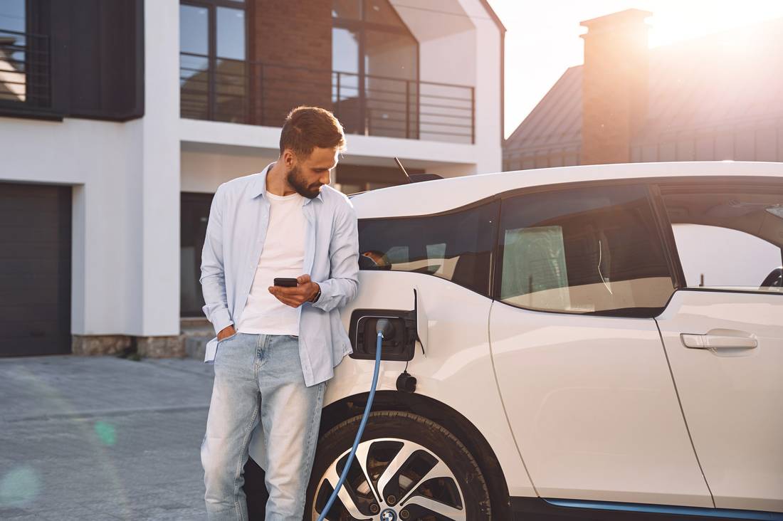 Man with smartphone leaning at electric car charging