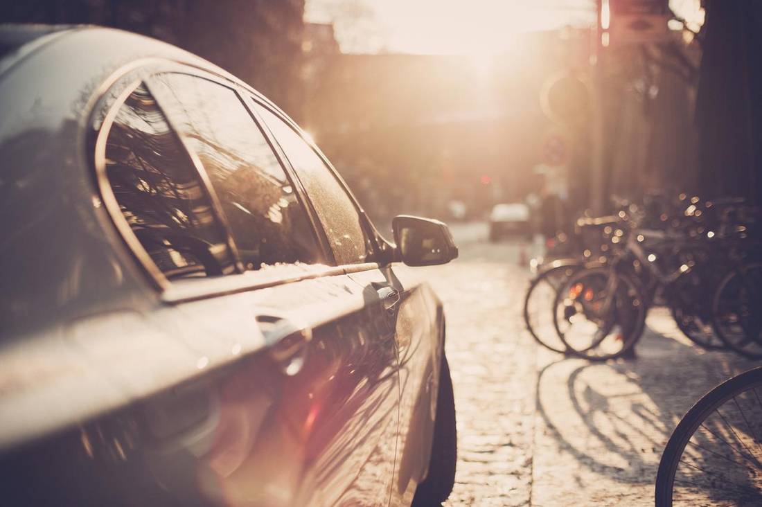 Side view of car driving against sun through city street